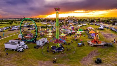 A drone photo of the 2026 Kyle Fair showing carnival rides, an open field, and people having fun with the sun setting in the background. 