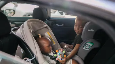 A photo of two young children in the back seat of a car. 